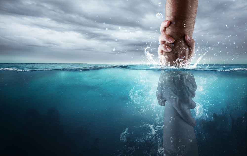 An image showing a hand reaching down into deep, choppy water to firmly grasp the forearm of a person submerged below the surface, symbolizing a rescue or a helping hand under a dark, cloudy sky.