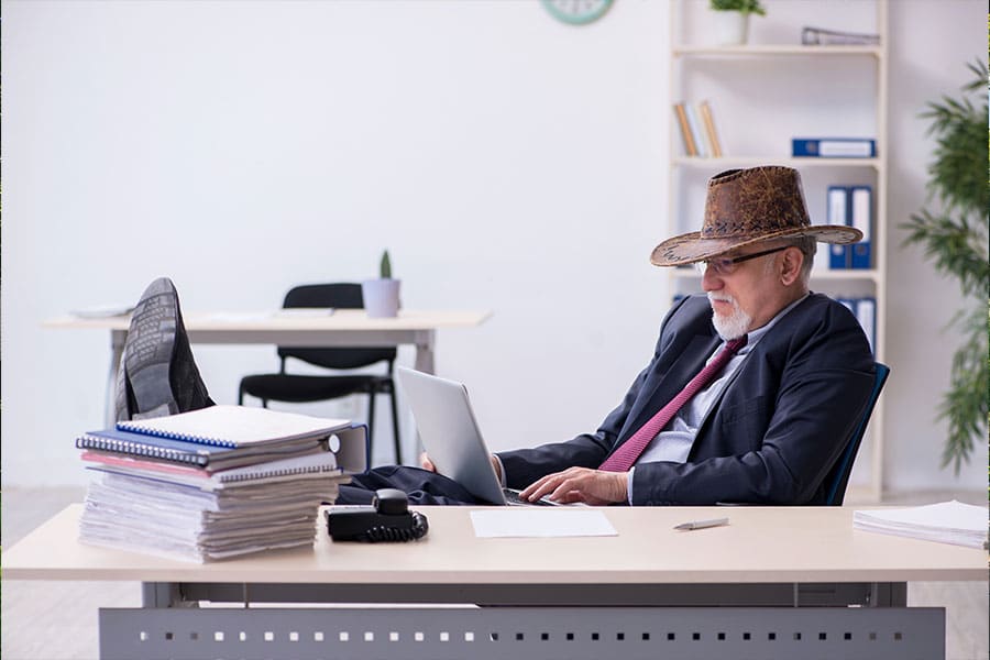 A mature male in a cowboy hat on a laptop with his feet on the desk representing Texas Comptroller.