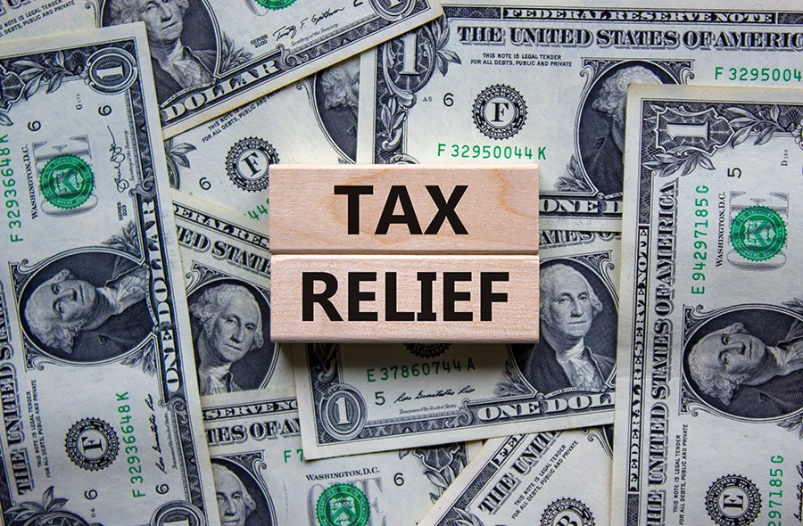 Two small wooden blocks with the words Tax Relief, on a pile of money (USD). Representing 1099 independent contractor tax relief.