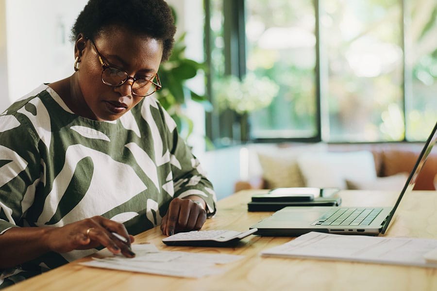 Dark-skinned woman handling taxes at the desk in front of her laptop.
